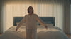 Woman falling back onto a large upholstered bed in a sunlit bedroom